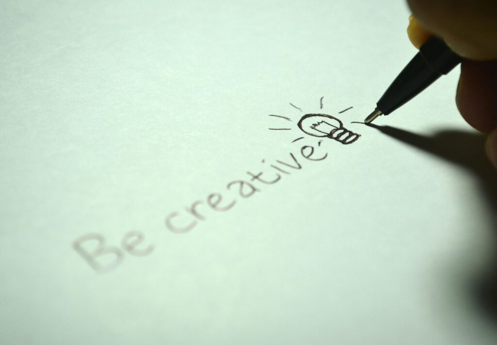 Close-up of handwritten 'Be creative' with a light bulb sketch on paper.